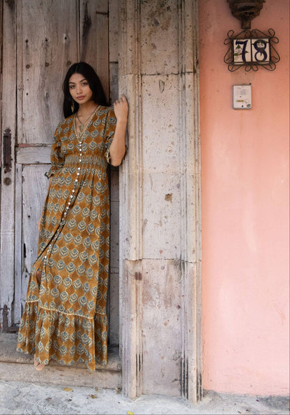 Woman in a patterned dress standing in front of a rustic wooden door with pink flowers above.