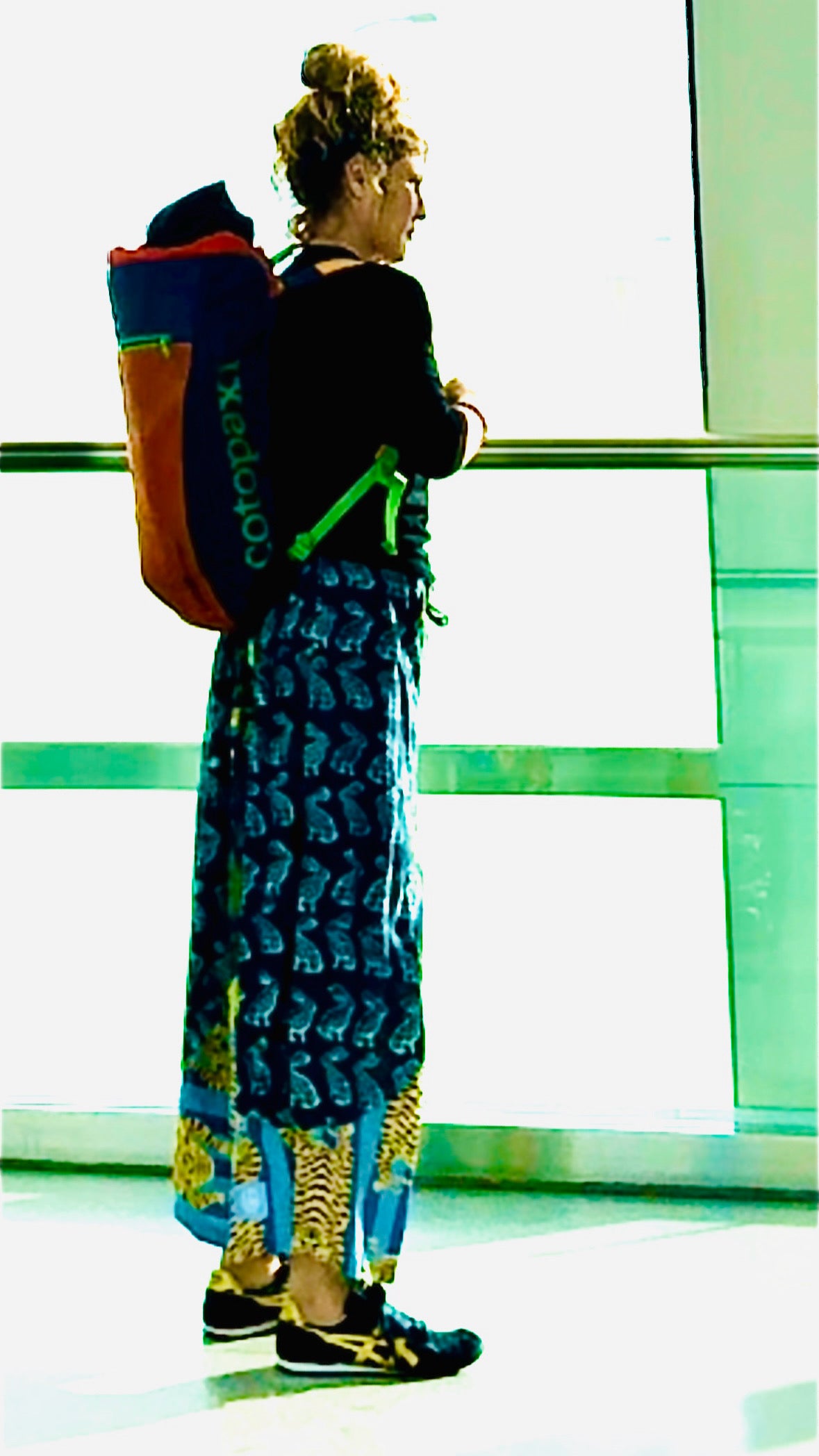 Person wearing a colorful backpack with a patterned dress, standing against a light background.