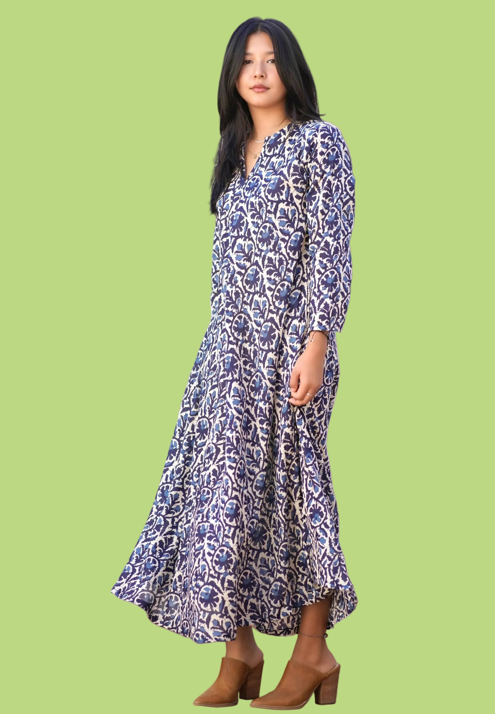 Woman wearing a blue floral dress standing in a room with a chair and plants.