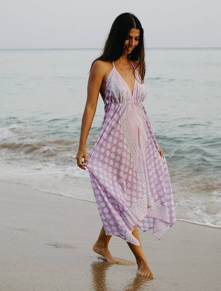 Woman in a purple dress walking on a beach with ocean waves in the background