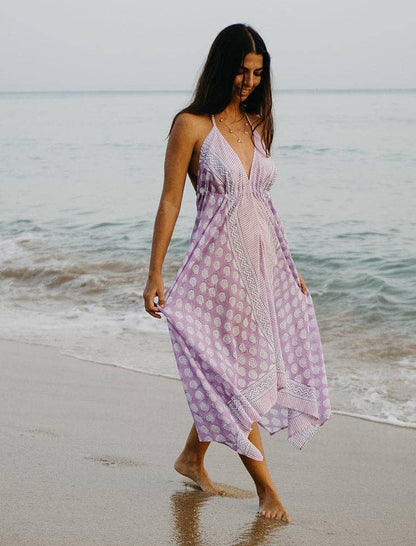 Woman in a purple dress walking on a beach with ocean waves in the background