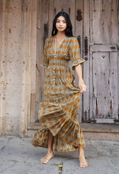 Woman in a patterned dress standing in front of a wooden door with pink flowers above.