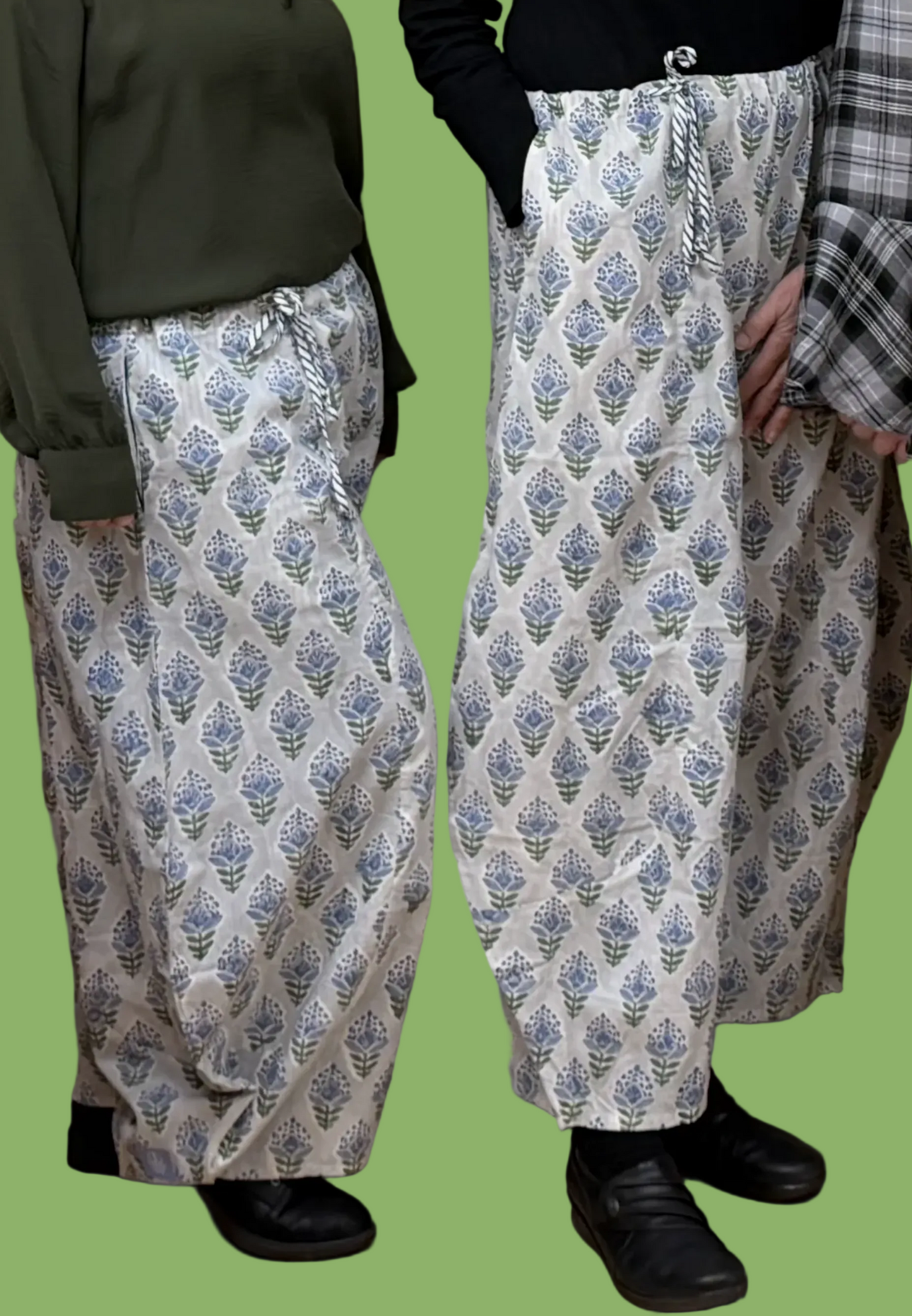 Two women wearing patterned pants standing against a wall.