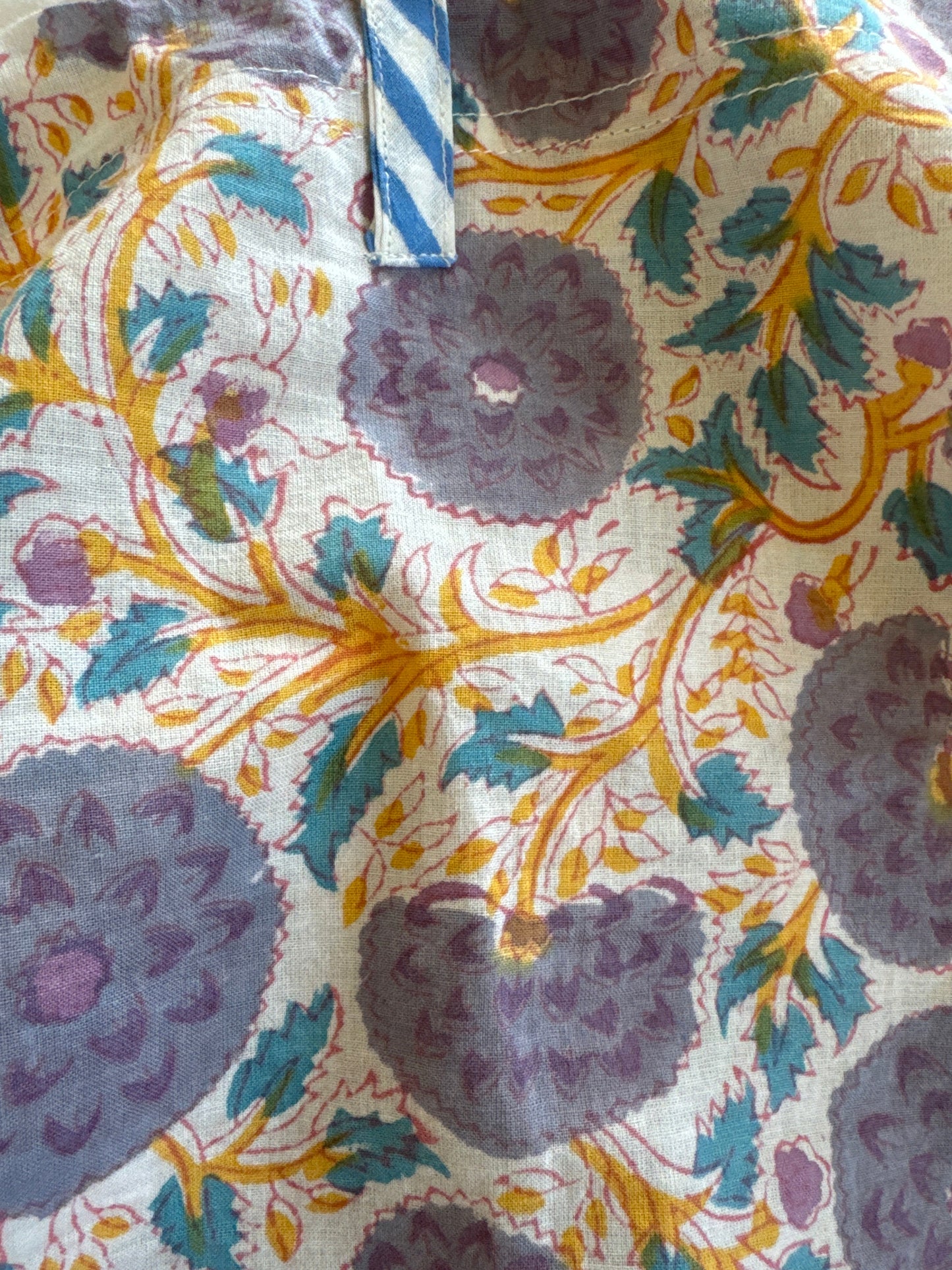 A person wearing a white top, blue patterned pants, a grey jacket, and a hat.