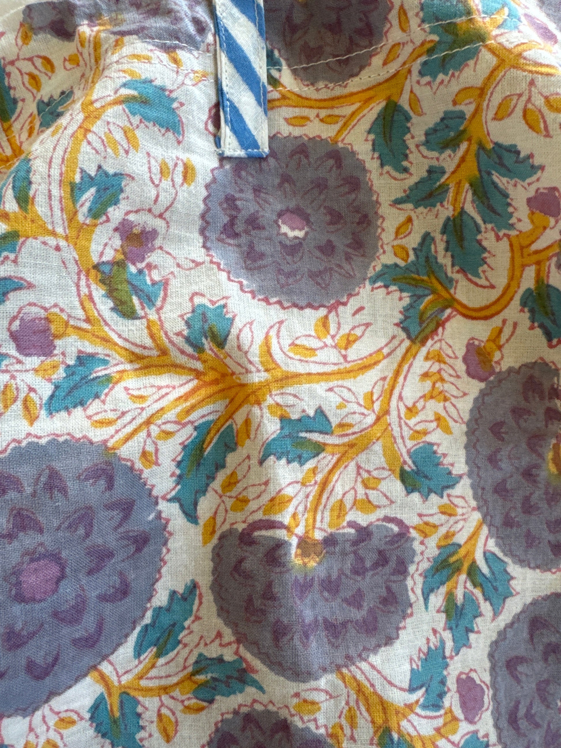 A person wearing a white top, blue patterned pants, a grey jacket, and a hat.