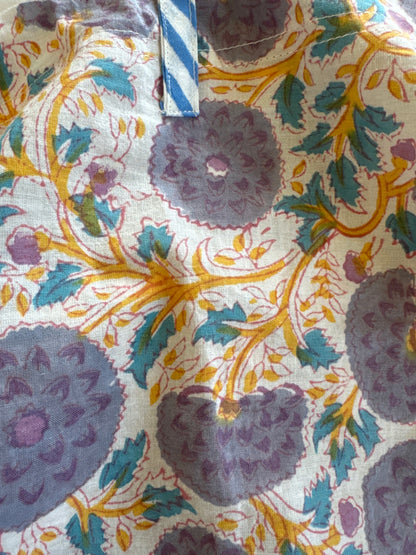 A person wearing a white top, blue patterned pants, a grey jacket, and a hat.