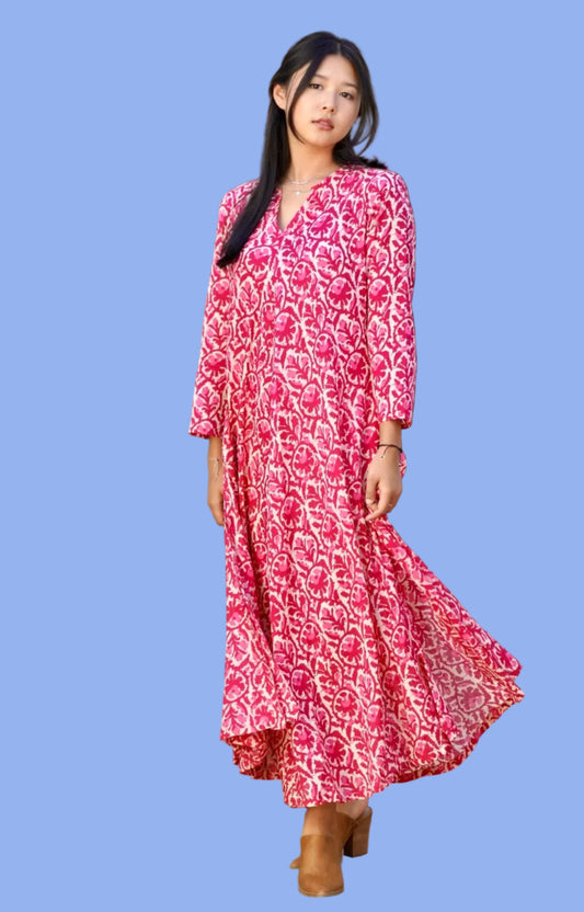 Woman wearing a red patterned dress standing in front of a white building with a glass door.