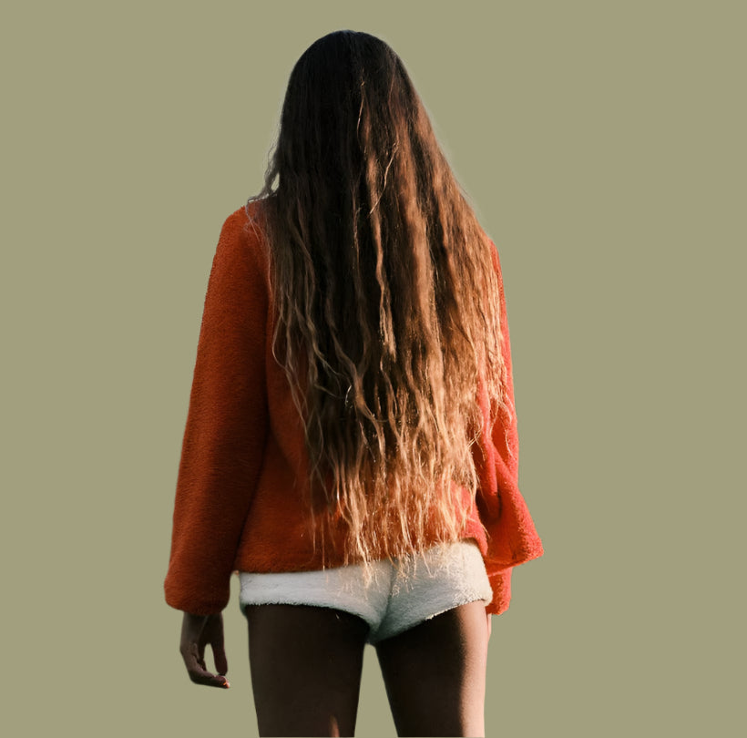 Person wearing an orange sweater and white shorts standing in a field with mountains in the background